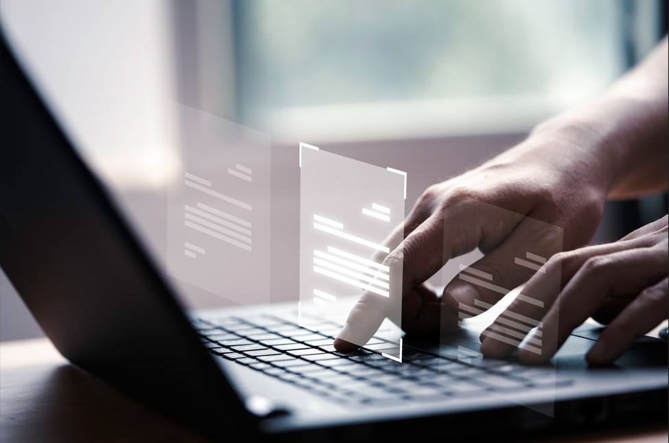 Mano usando una computadora portatil con pantalla virtual y documentos para ejemplificar documentos en soporte digital. Autoría: FREEPIK.es